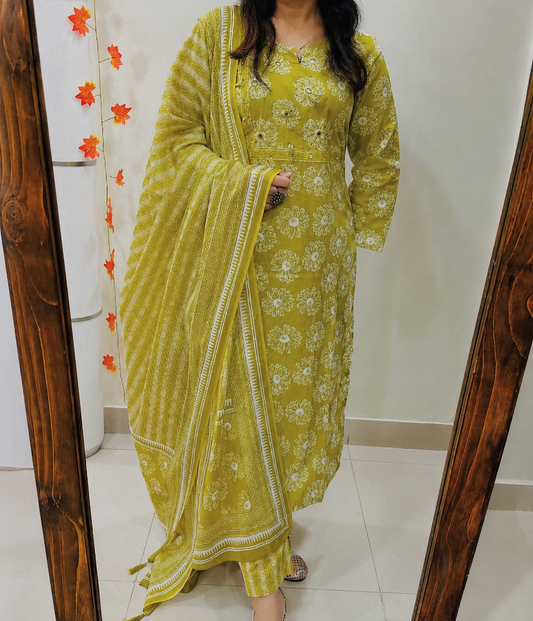 A woman wearing a yellow-green kurta set with white floral prints and a matching dupatta, standing in front of a mirror in an indoor setting.