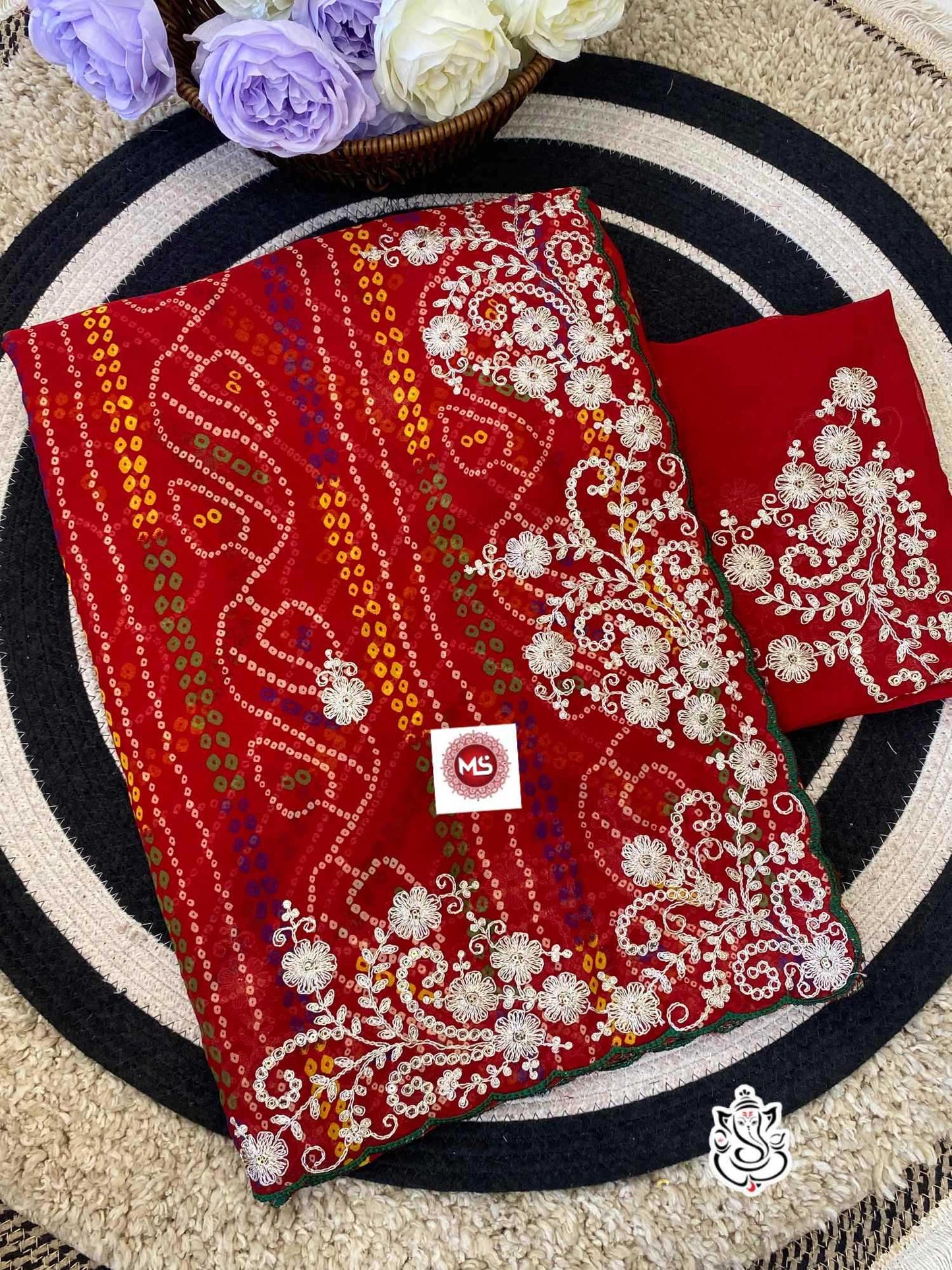 Red embroidered fabric with white patterns on a circular mat with flowers in the background