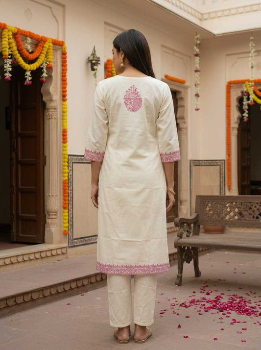 Woman in a white traditional outfit standing in a decorated indoor setting with floral decorations.