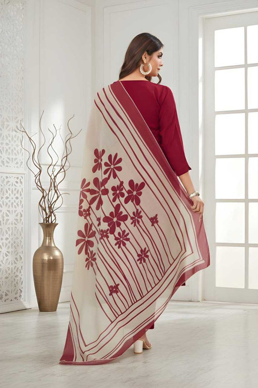 Woman wearing a maroon saree with floral patterns in a bright room.