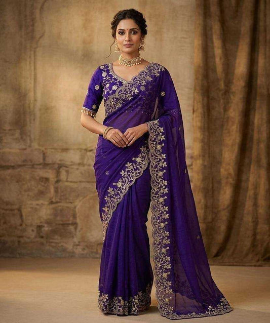 Woman wearing a purple saree with silver embroidery against a textured brown background