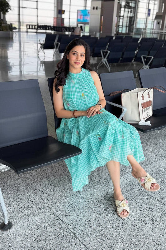 Woman in a teal dress sitting in an airport terminal holding a red cup.