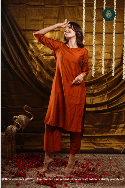 Woman in an orange outfit standing against a decorative backdrop with floral decorations.