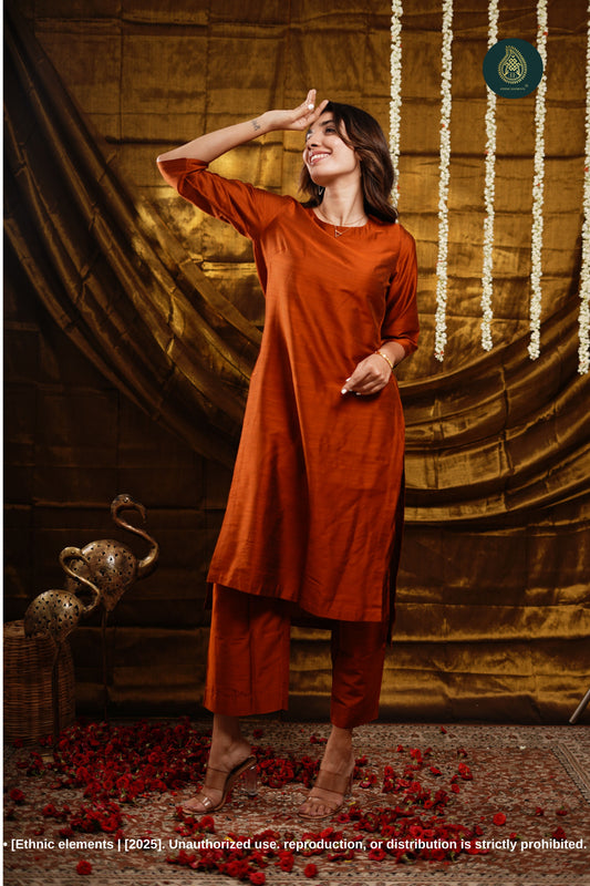 Woman in an orange outfit standing against a decorative backdrop with floral decorations.