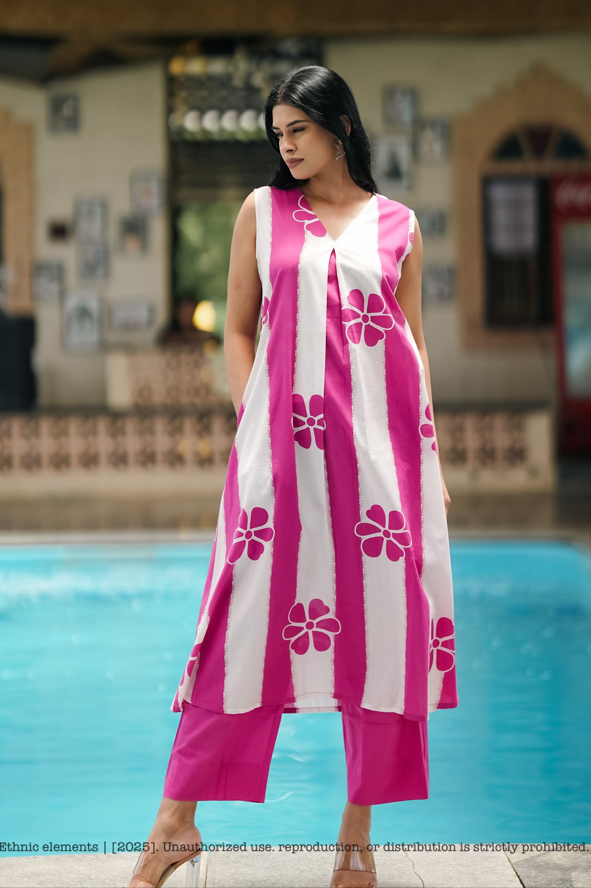 Woman in a pink and white floral dress standing by a pool.