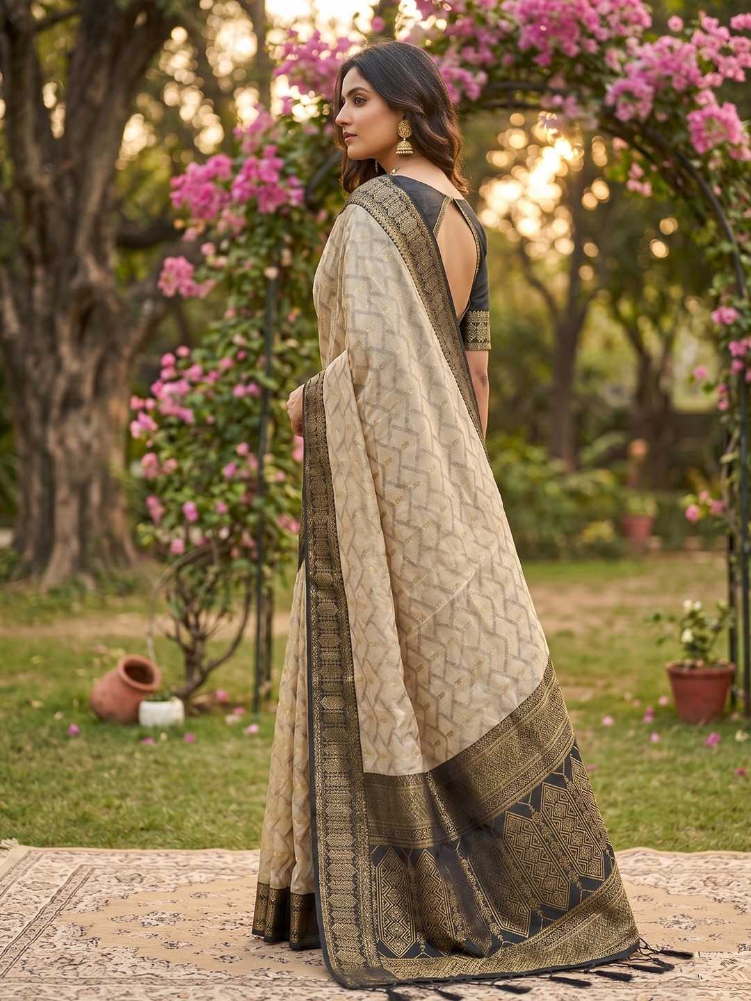 Woman in a traditional saree standing in a garden with pink flowers and greenery.