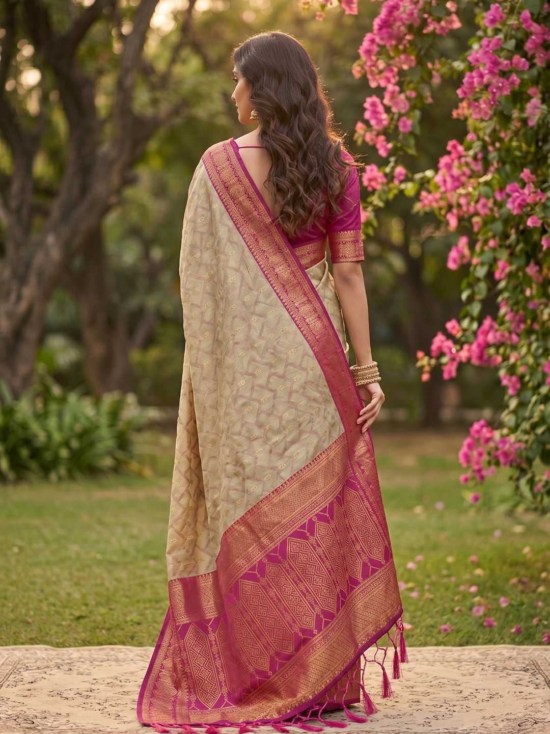 Woman in a traditional saree standing in a garden with pink flowers and greenery.