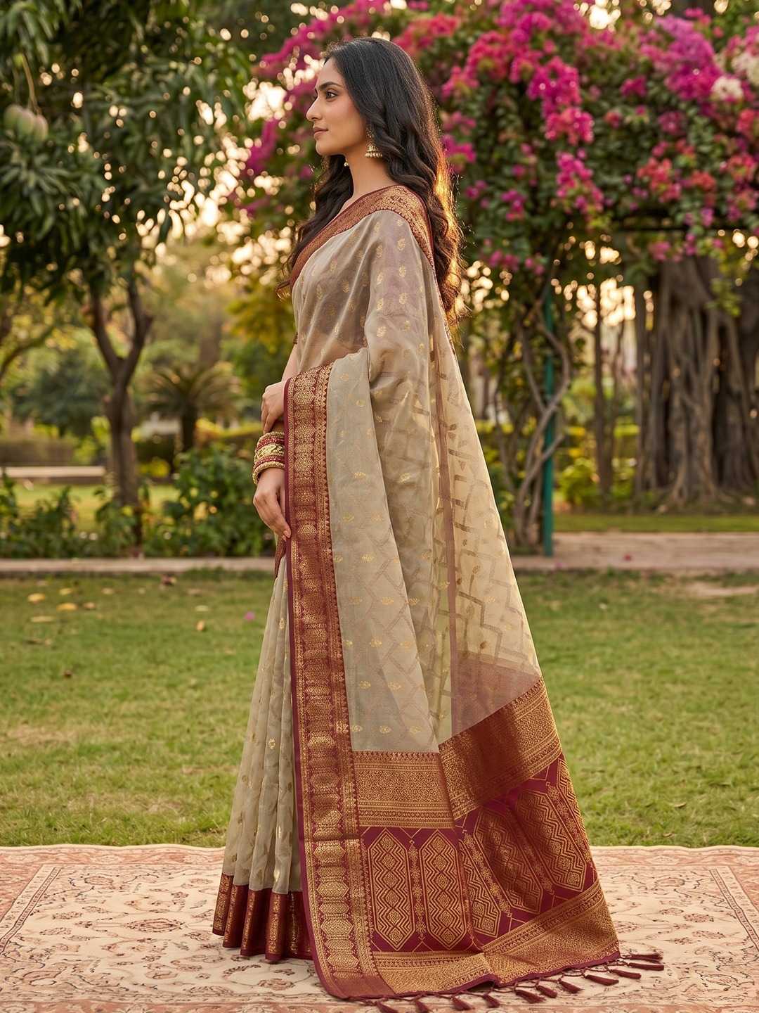 Woman in a traditional saree standing in a garden with flowers and greenery.