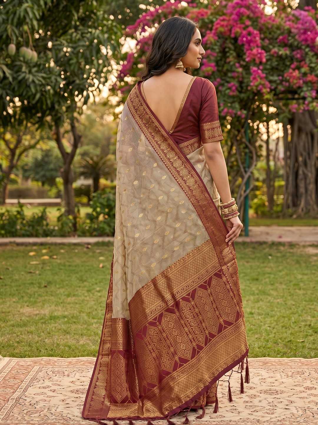 Woman wearing a traditional saree in an outdoor setting with greenery and flowers.