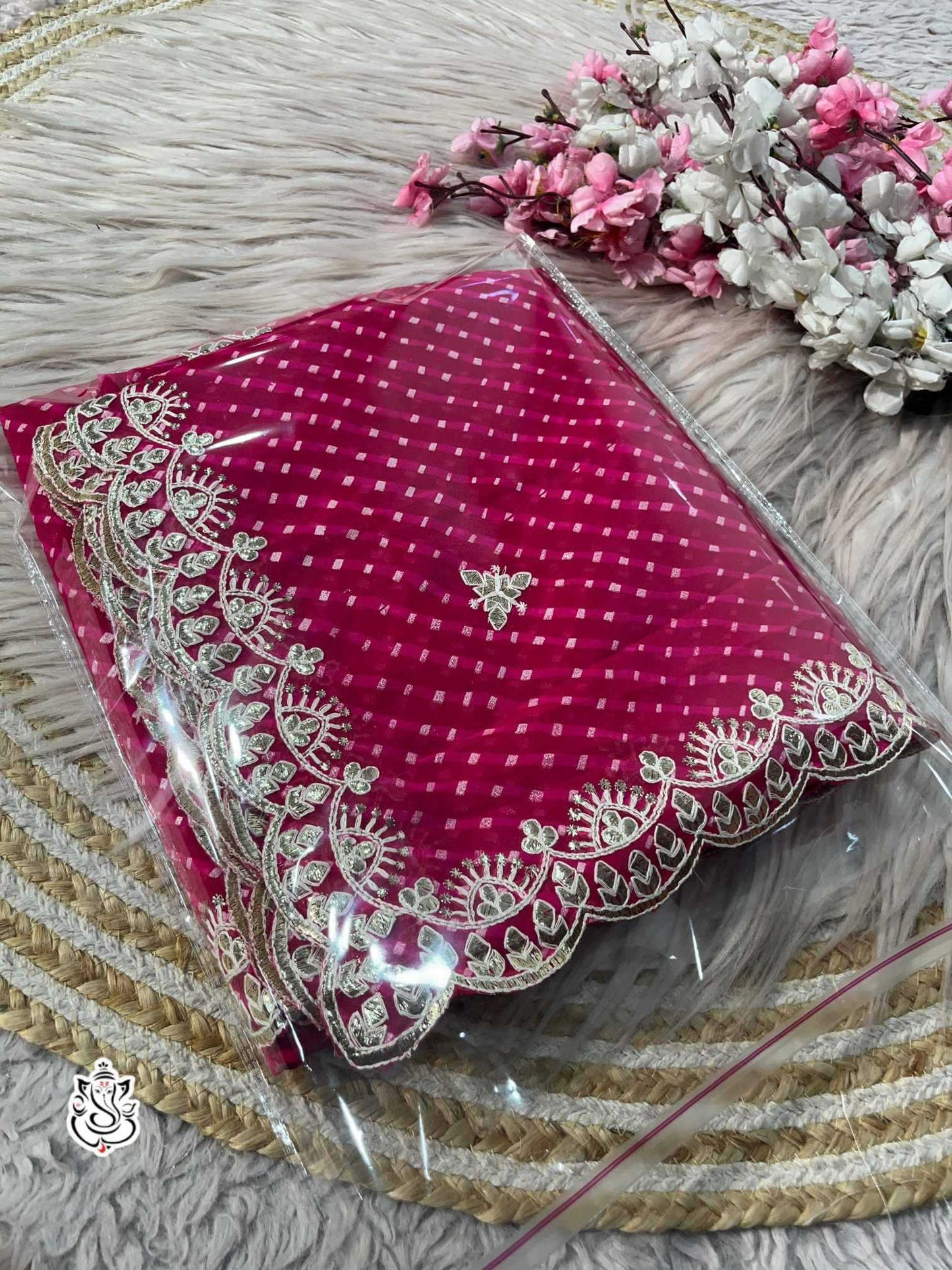 Pink fabric with intricate white embroidery on a textured surface with flowers.