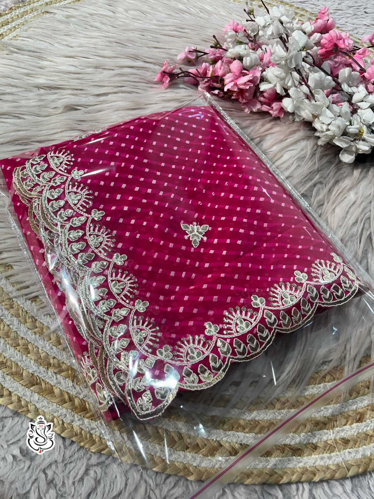 Pink fabric with intricate white embroidery on a textured surface with flowers.