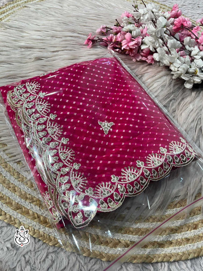 Pink fabric with intricate white embroidery on a textured surface with flowers.