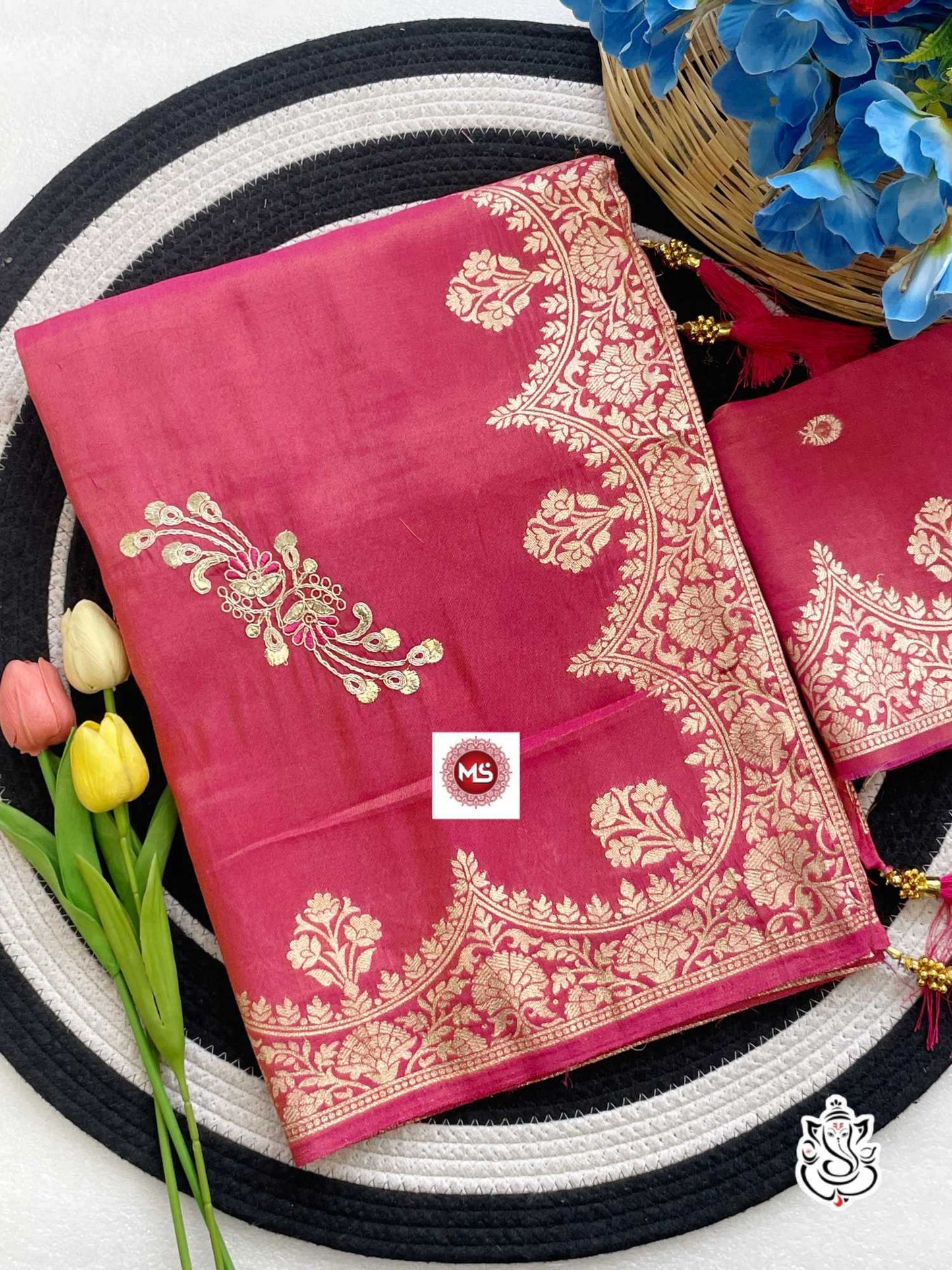 Pink saree with gold embroidery on a white and black striped background with flowers.