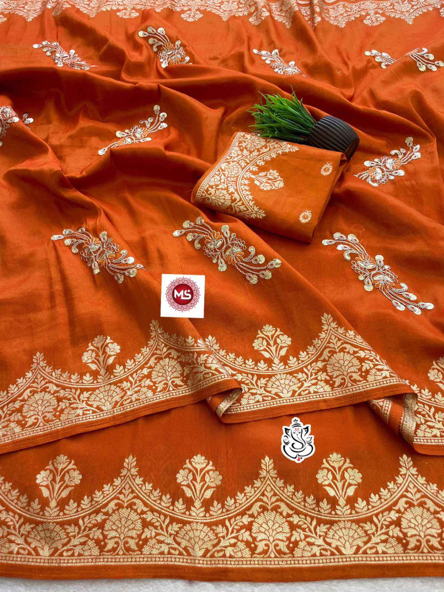 Orange saree with white embroidery and a brand logo on a light gray background