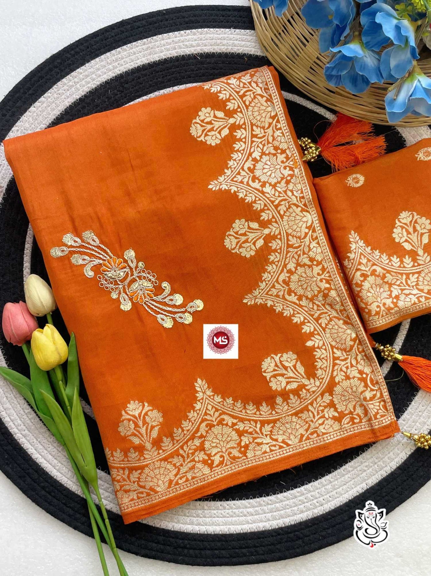 Orange fabric with gold embroidery on a circular black and white mat with flowers.