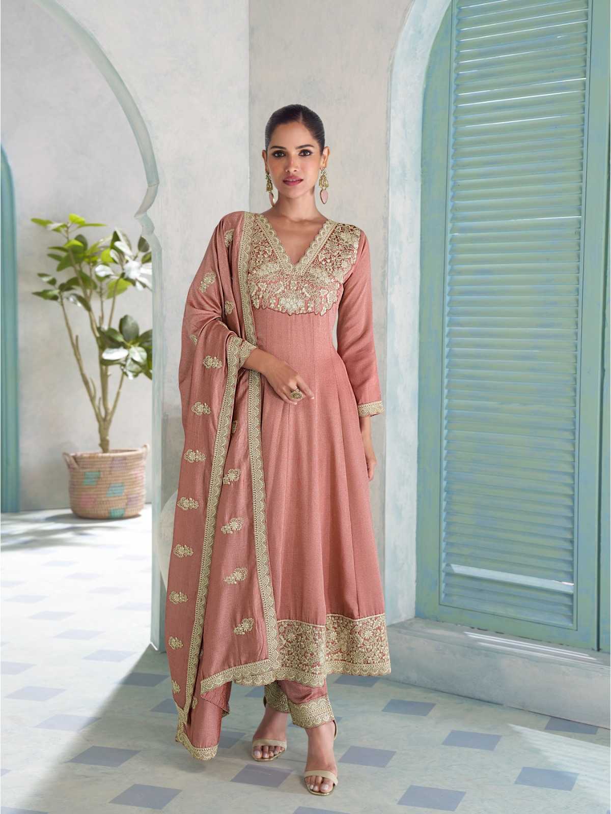 Woman in a pink traditional outfit with gold embroidery standing in a room with light blue shutters.