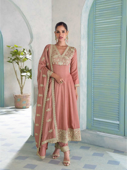 Woman in a pink traditional outfit with gold embroidery standing in a room with light blue shutters.