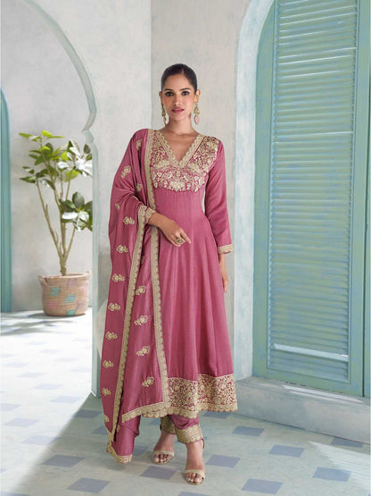 Woman in a pink traditional outfit with gold embroidery standing in a light-colored room.