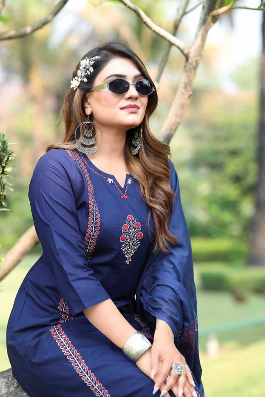 Woman in a blue embroidered dress sitting outdoors with greenery in the background