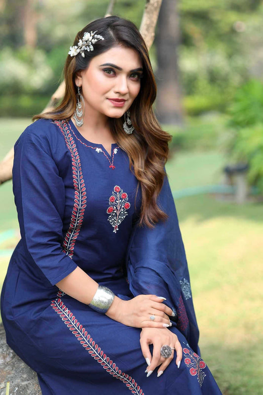 Woman wearing a blue embroidered dress sitting outdoors with greenery in the background