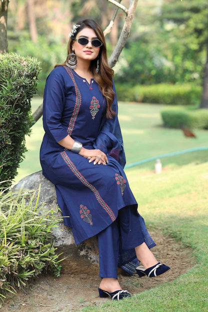 Woman in a blue embroidered outfit sitting on a rock in a garden