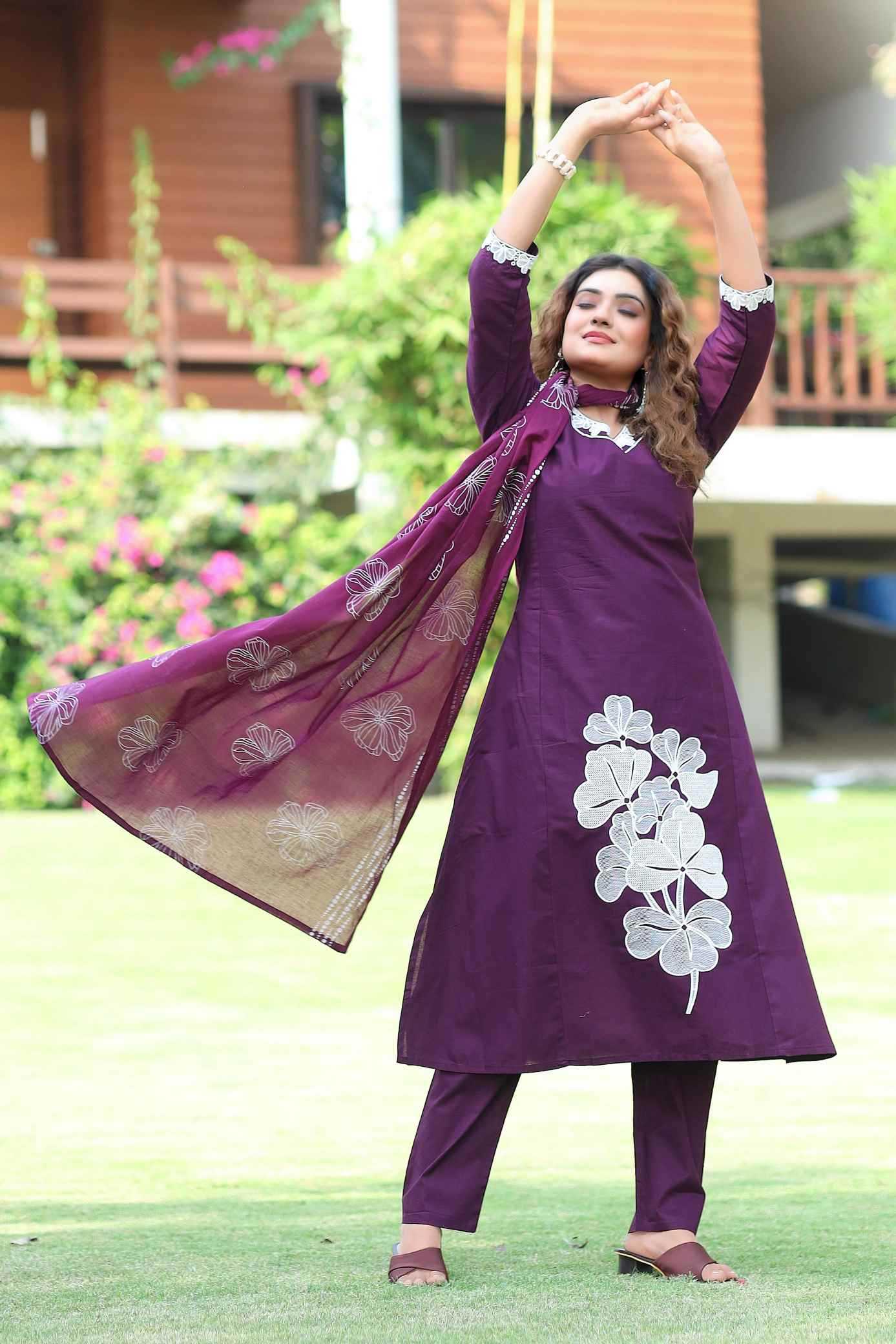 Woman in a purple traditional outfit with floral patterns standing outdoors.