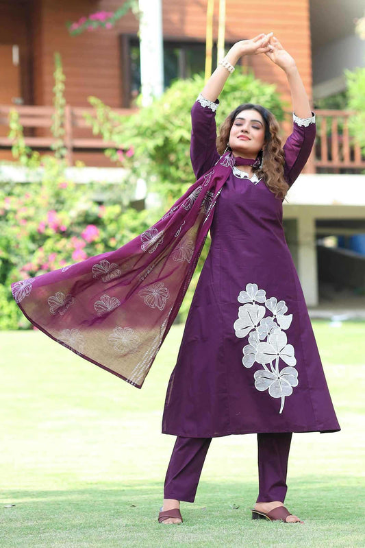 Woman in a purple traditional outfit with floral patterns standing outdoors.