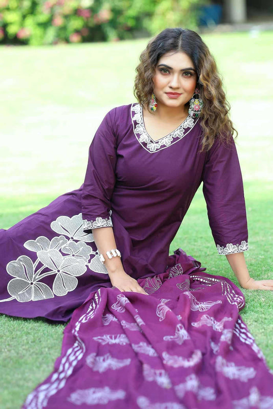 Woman in a purple traditional outfit with white patterns sitting on grass.