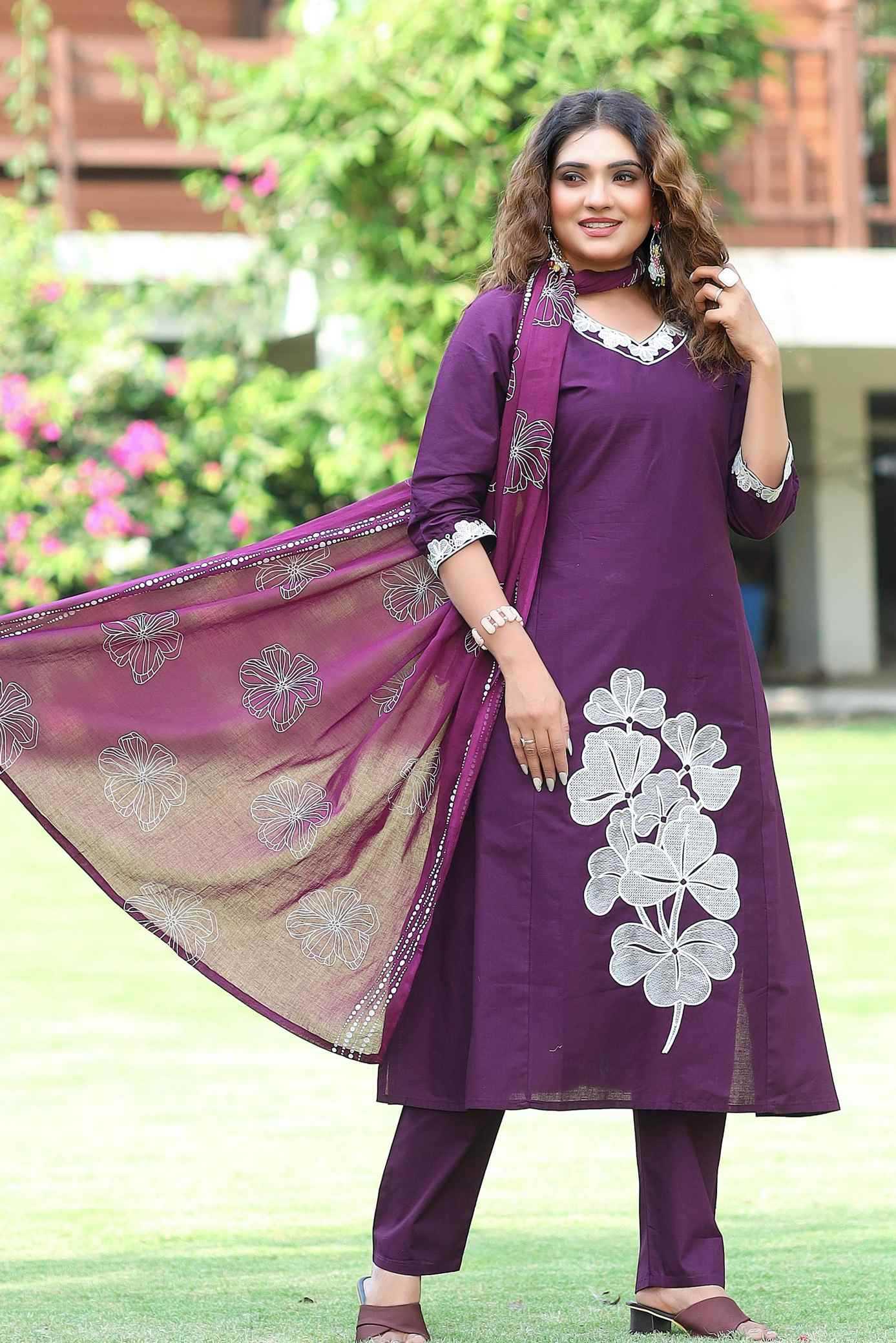 Woman wearing a purple traditional outfit with floral patterns in an outdoor setting.