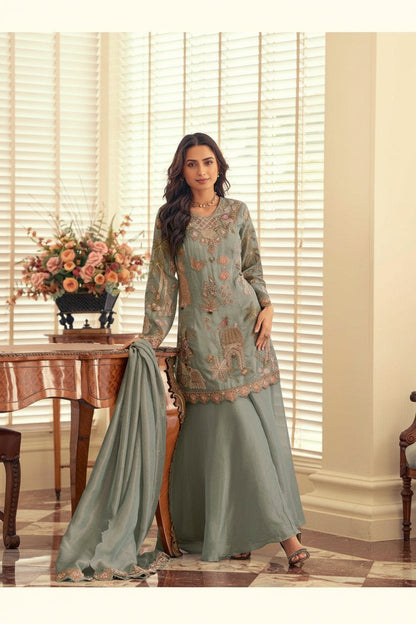 Woman in a light green embroidered outfit standing in a room with a table and flowers.