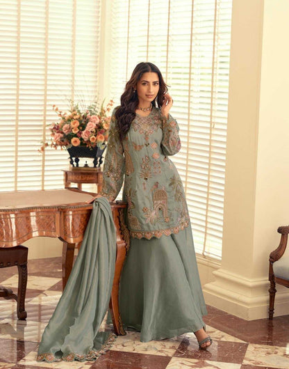 Woman in a traditional outfit standing in a room with a table and flowers.
