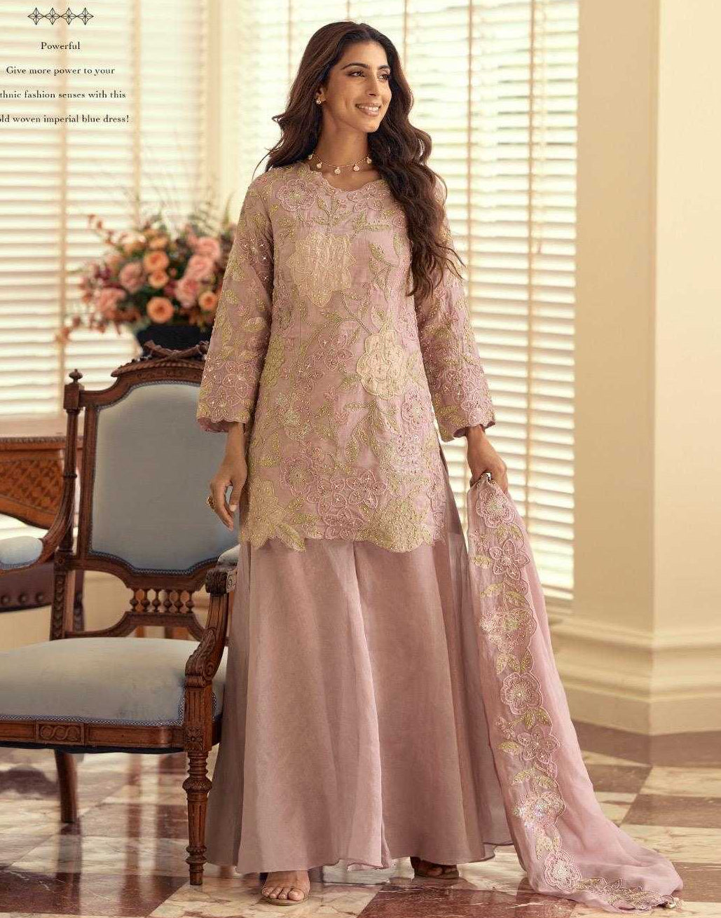 Woman in a pink traditional outfit standing in a room with a dining table and floral arrangement.