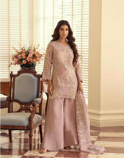 Woman in a traditional outfit standing in a room with a chair and flowers.