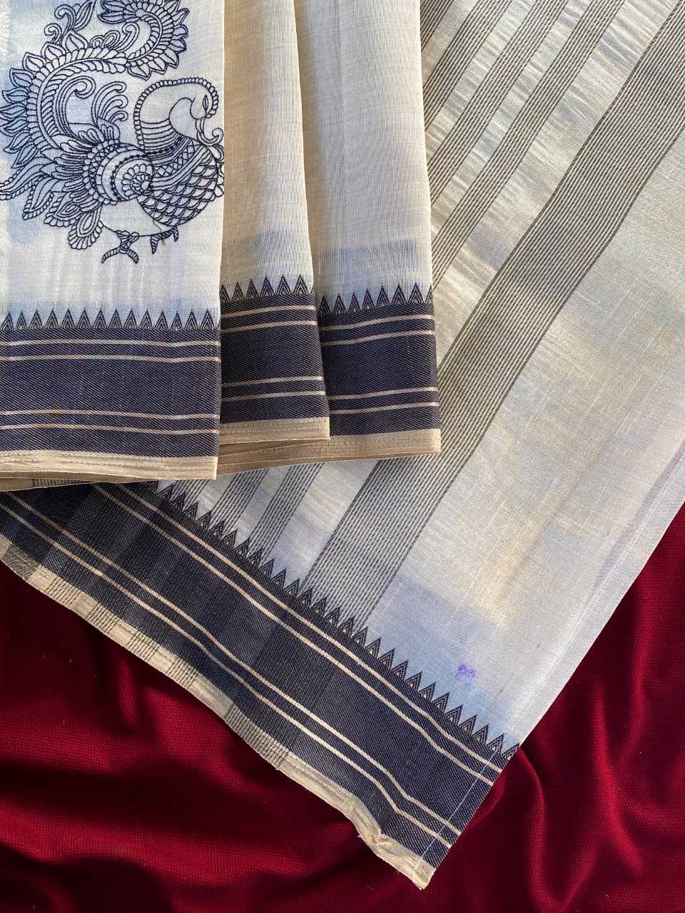 A close-up of a folded white and light gray striped fabric with dark navy borders, a printed peacock motif on the left, and a deep red satin-like fabric underneath.
