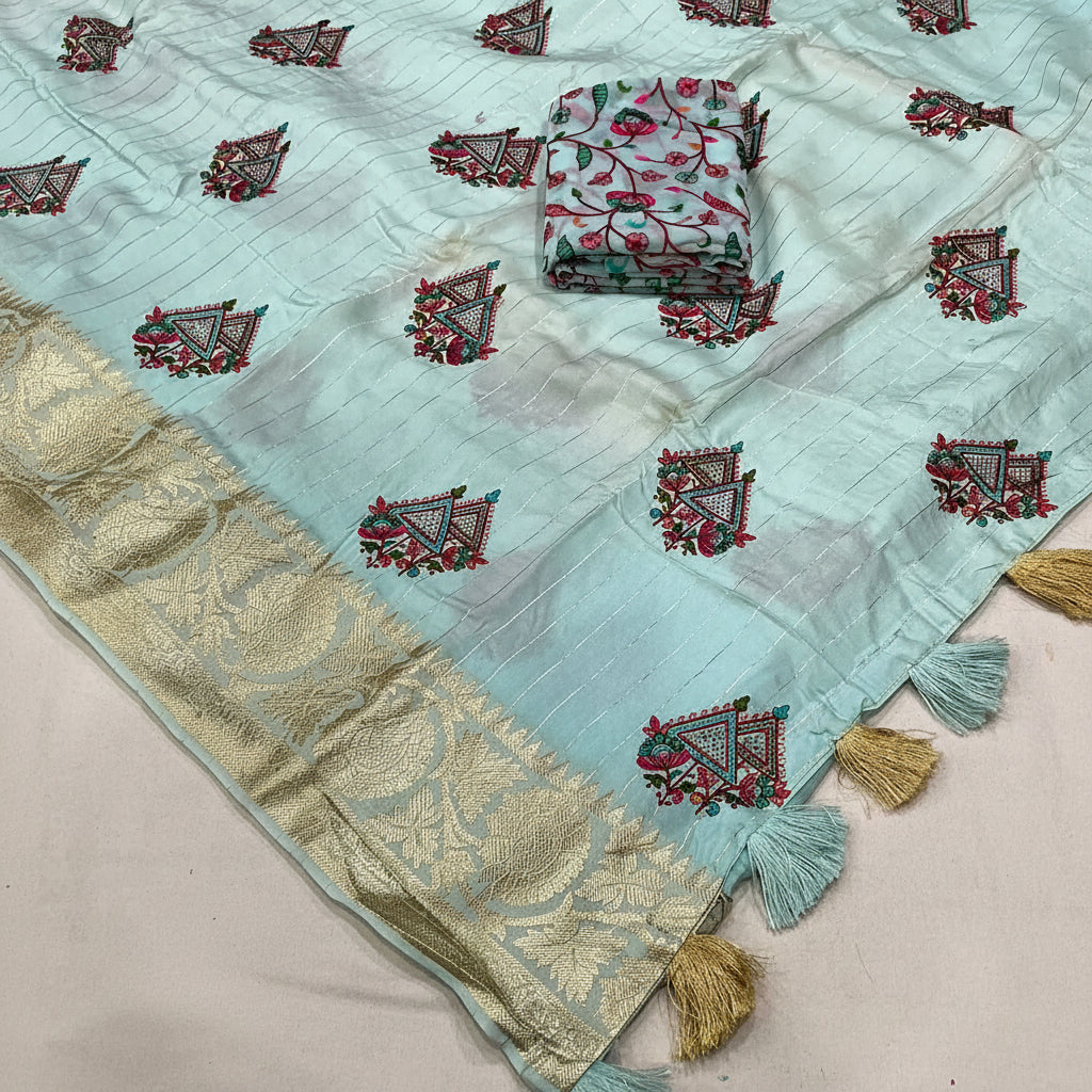 A light sky blue georgette fabric saree with embroidered motifs and a gold zari border, displayed flat with a folded matching fabric piece on top and tassels along the edge.