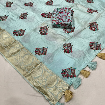 A light sky blue georgette fabric saree with embroidered motifs and a gold zari border, displayed flat with a folded matching fabric piece on top and tassels along the edge.