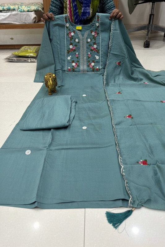 Teal embroidered traditional outfit with a person holding it, displayed on a light-colored floor.