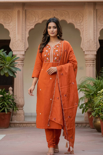 Woman wearing an orange traditional outfit with embroidery in a decorative setting.