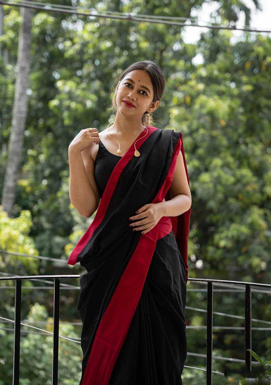 Woman in a black and red saree standing outdoors with greenery in the background