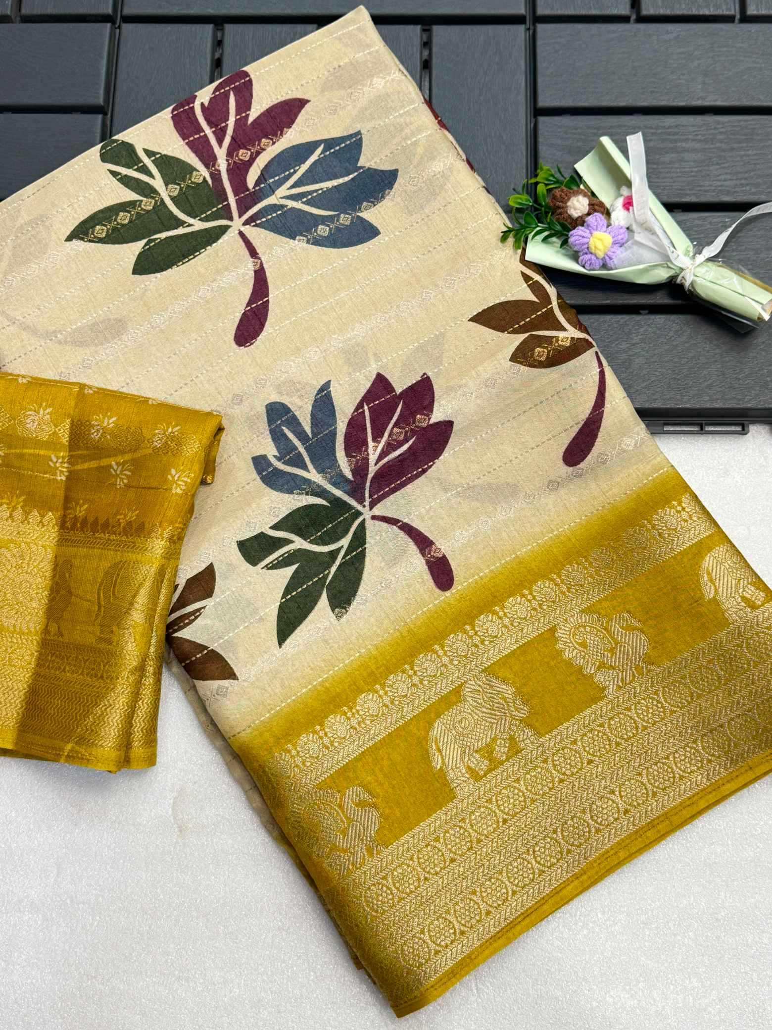 Beige saree with leaf patterns and a yellow border on a white surface.