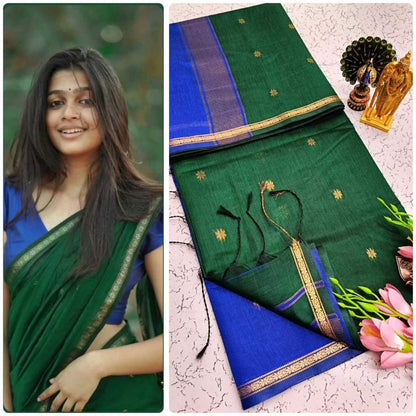 Woman wearing a green and blue saree with floral decorations on a textured surface.