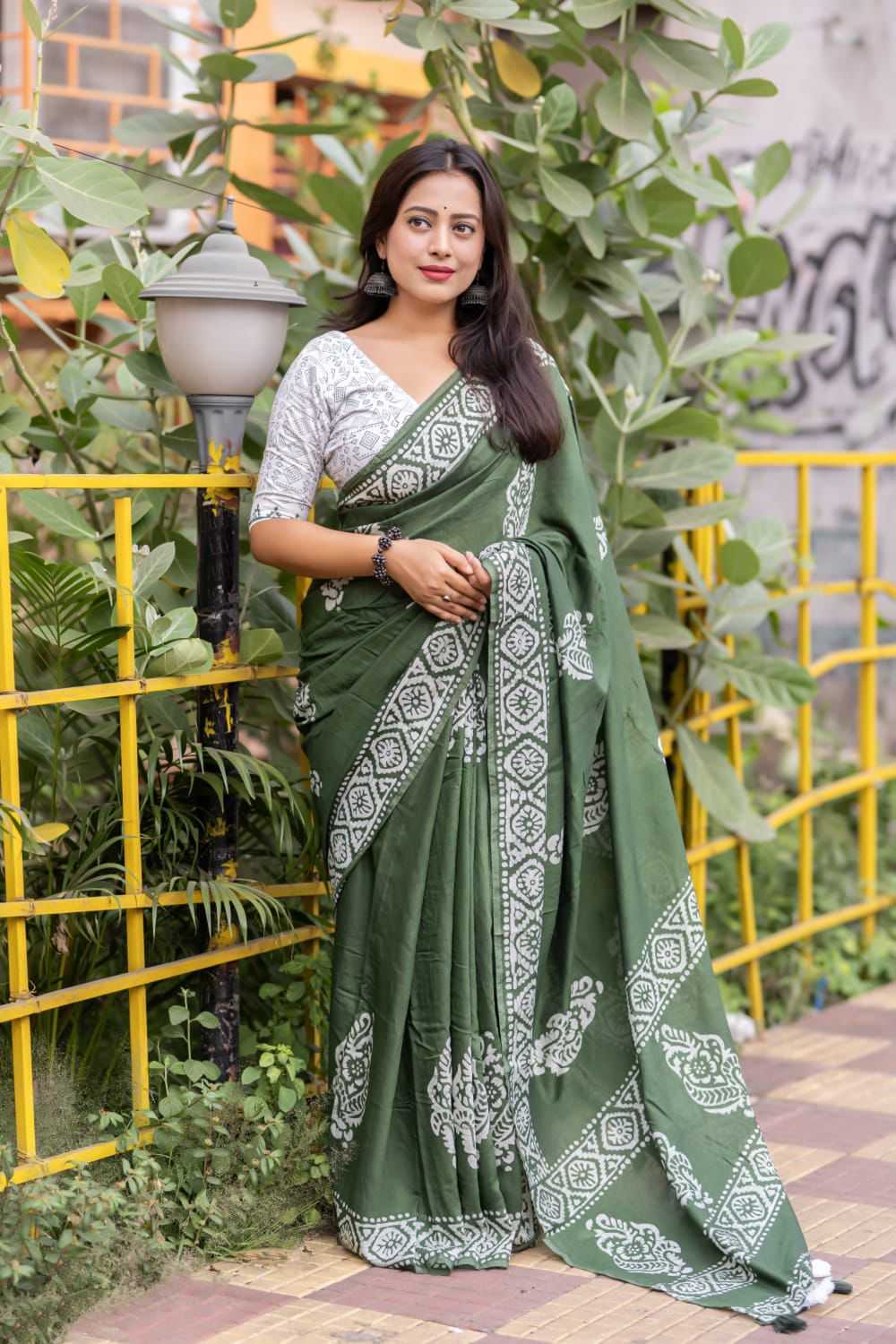Woman in a green saree with white patterns standing outdoors.