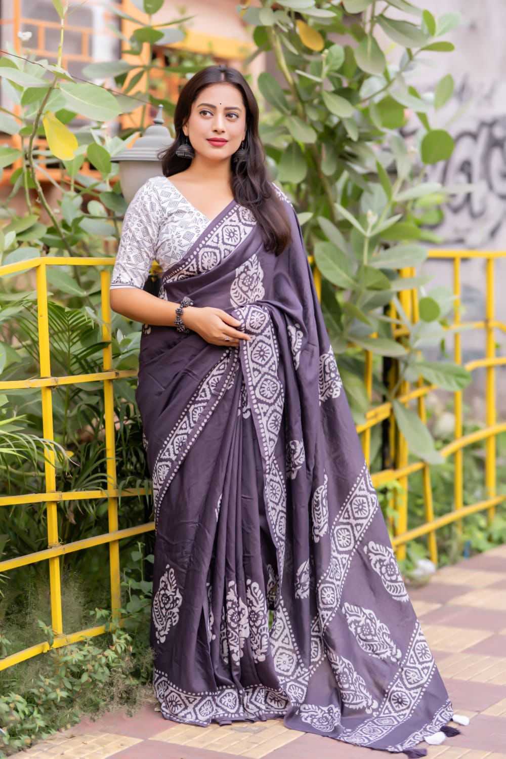 Woman wearing a dark purple saree with white patterns standing outdoors.