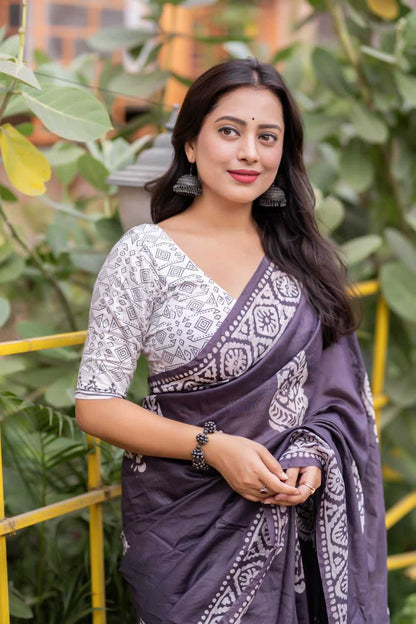 Woman wearing a traditional saree with a white blouse and purple saree in an outdoor setting.
