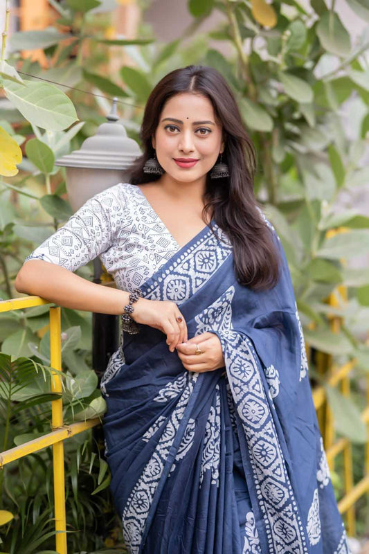 Woman wearing a blue saree with white patterns against a green foliage background