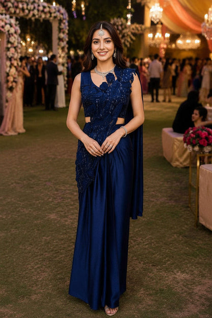 Woman in a blue evening gown at an outdoor event with decorations and people in the background.