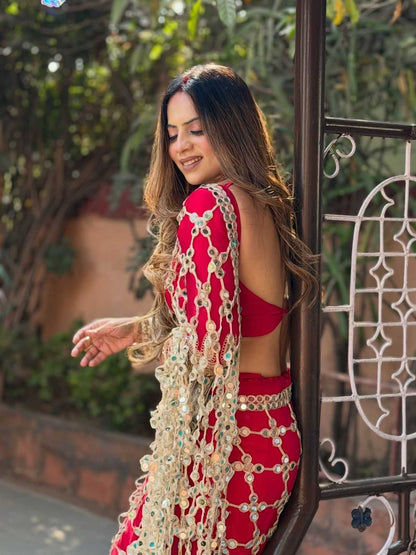 Woman in a red and gold traditional outfit standing outdoors with greenery in the background