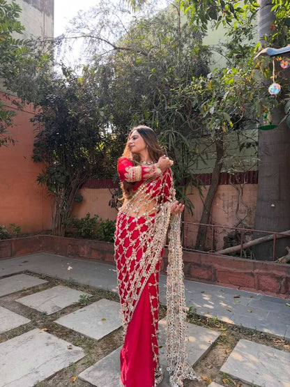 Woman in a red saree with gold details standing outdoors.
