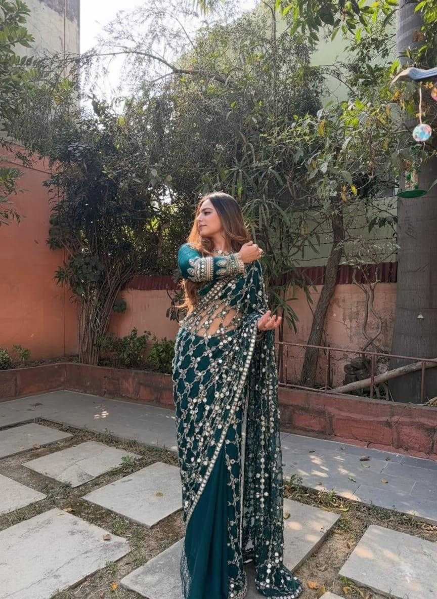 Woman in a traditional saree standing outdoors with greenery and a building in the background