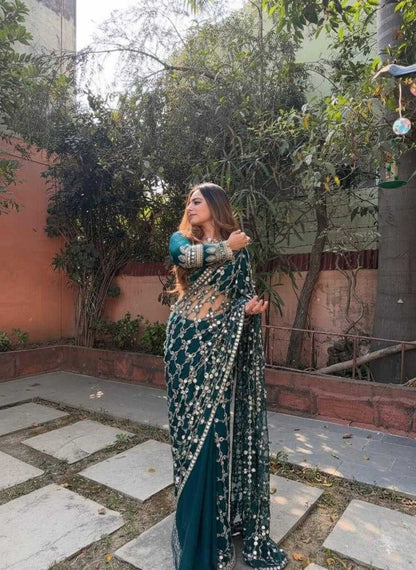 Woman in a traditional saree standing outdoors with greenery and a building in the background